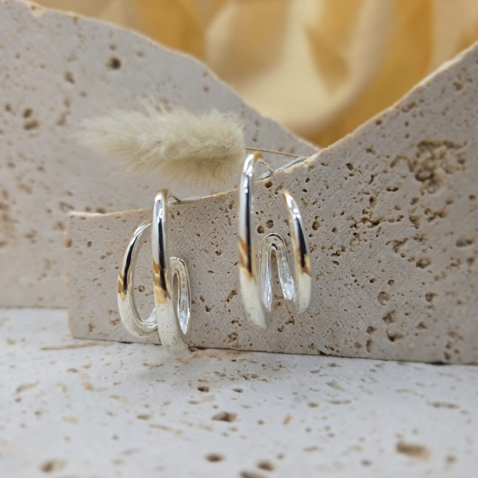 Silver hoop earrings on a textured stone surface with a blurred floral background