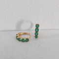 Gold hoop earrings with green gemstones on a light gray background