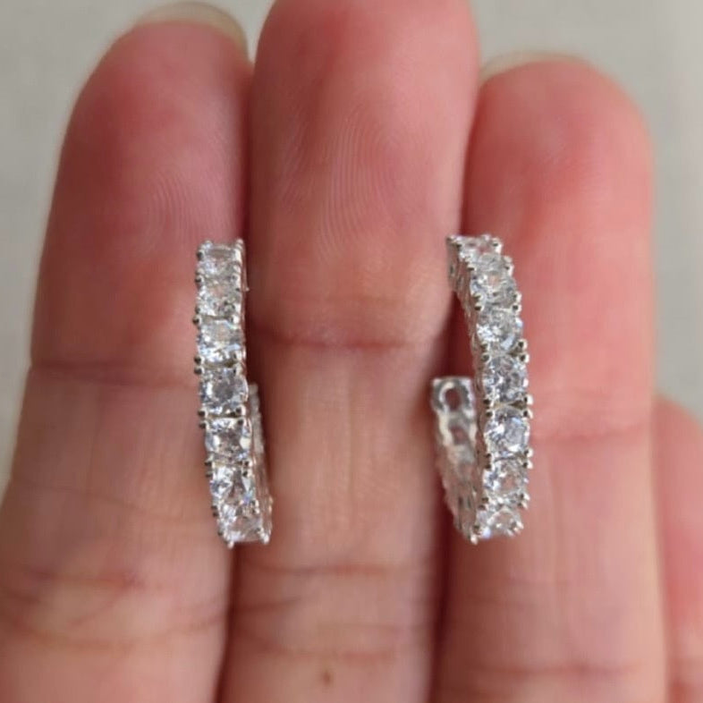 Diamond earrings held between fingers against a neutral background