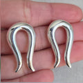 Pair of silver earrings held between fingers on a neutral background