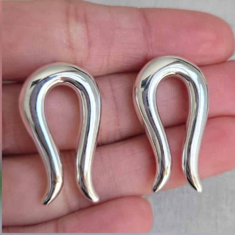 Pair of silver earrings held between fingers on a neutral background