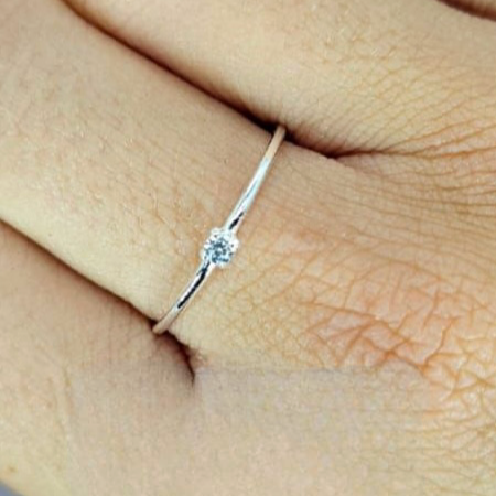 A person's hand displaying a petite sterling silver ring with a cubic zirconia on their finger.