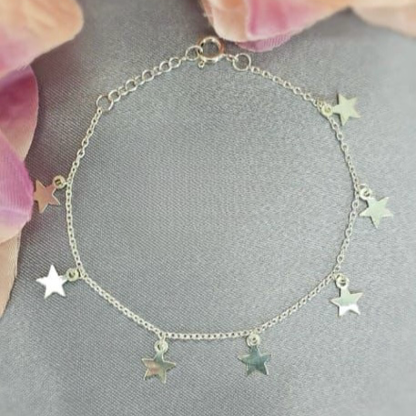 A silver bracelet with dangling star charms placed on a flat surface with a floral background.