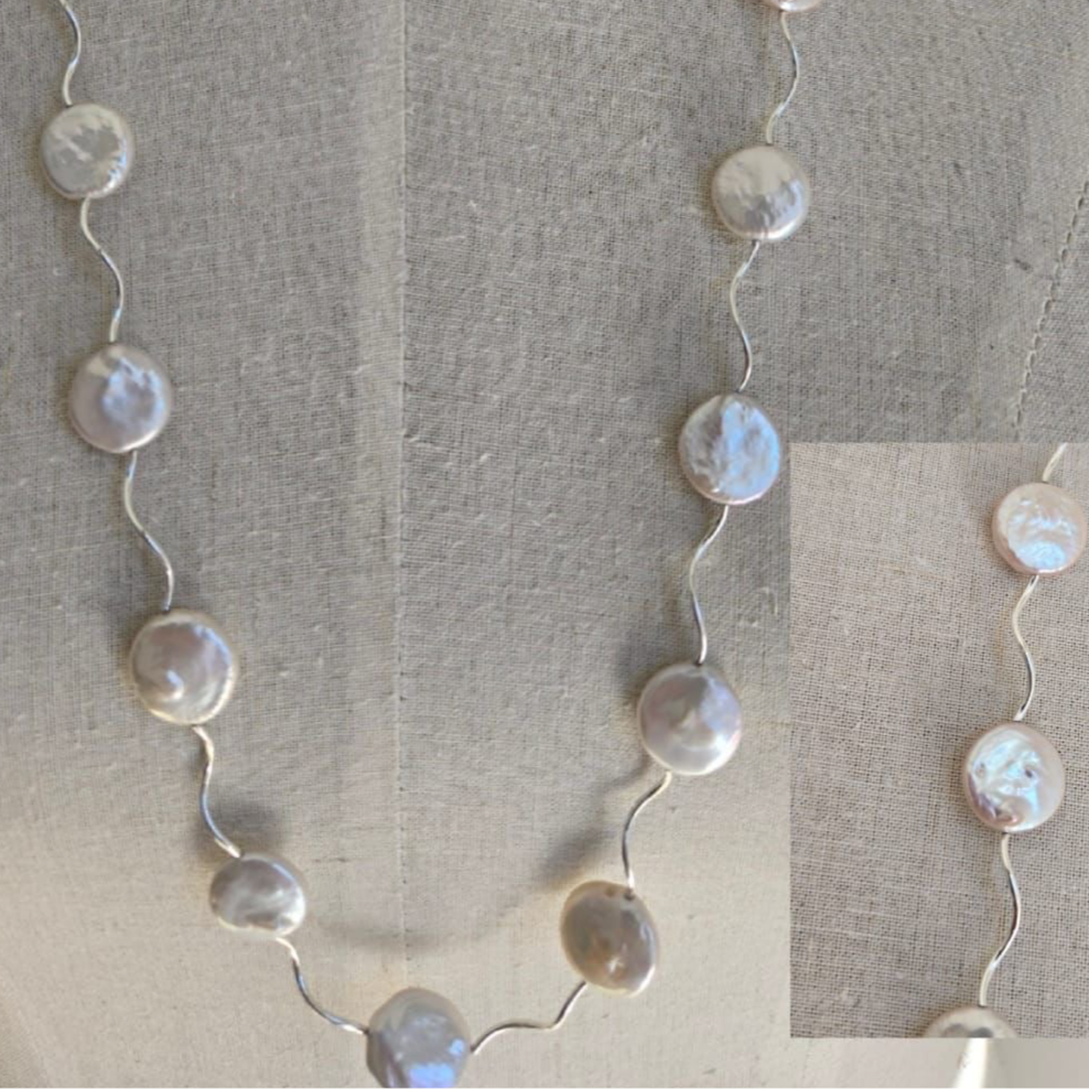 A long coin pearl necklace with a silver chain, displayed on a mannequin.