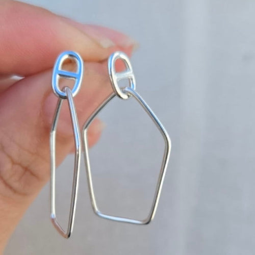 Silver earrings held by a hand against a plain background