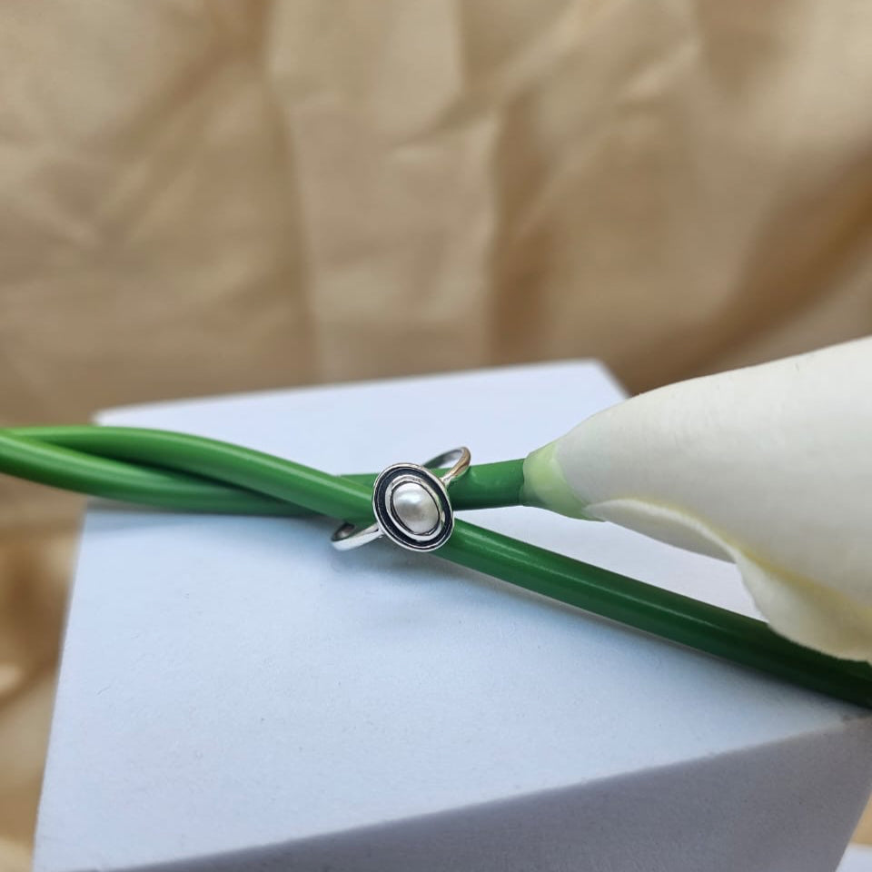 Silver ring with a pearl on a green cord against a beige background