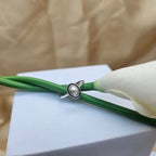 Silver ring with a pearl on a green cord against a beige background