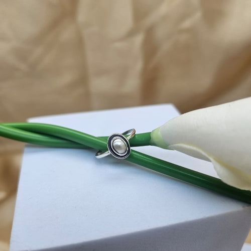 Silver ring with a pearl on a green cord against a beige background