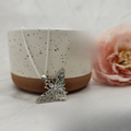 A sterling silver bee pendant with intricate details, displayed on a white surface next to a pink flower.