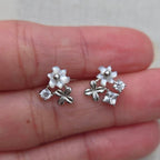 Silver earrings with floral designs held between fingers on a light background