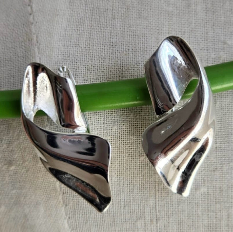Silver earrings on a green straw against a beige fabric background