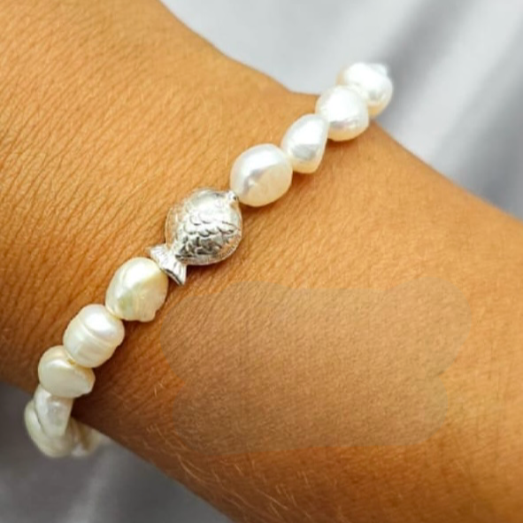A sterling silver fish inset bracelet with freshwater pearls on a person's wrist.