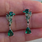 Green gemstone earrings held between fingers against a blurred background