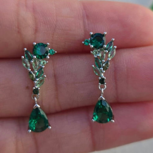 Green gemstone earrings held between fingers against a blurred background