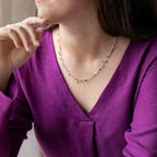 A person wearing a purple top is showcased wearing a sterling silver necklace with tourmaline semi-precious stones dangling on it.