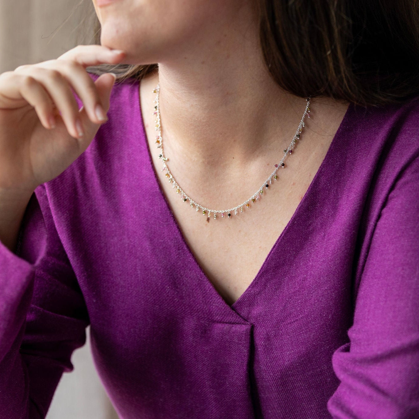A person wearing a purple top is showcased wearing a sterling silver necklace with tourmaline semi-precious stones dangling on it.