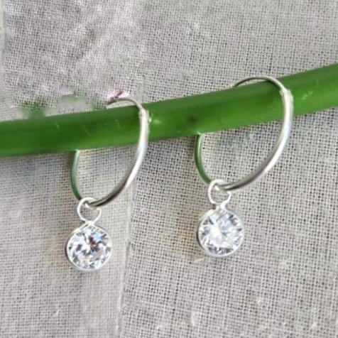 Silver hoop earrings with clear gemstones on a textured fabric background