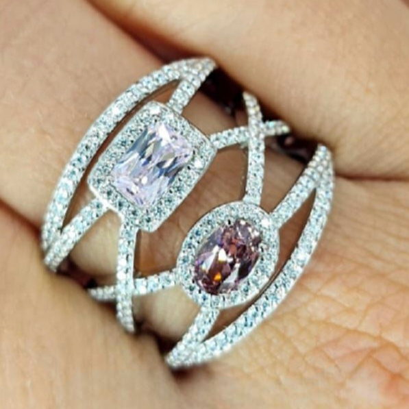 A sterling silver ring with a crisscross design featuring shades of pink cubic zirconia, adorned with small diamonds.