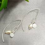 A pair of sterling silver drop earrings with pearl charms, displayed on a grey background with a green plant in the background.