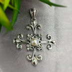 A sterling silver cross pendant with a central pearl, featuring intricate details and a decorative border.