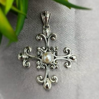 A sterling silver cross pendant with a central pearl, featuring intricate details and a decorative border.