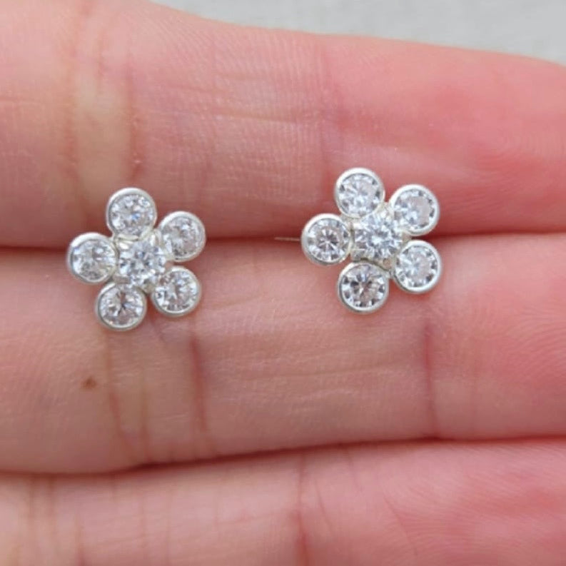 Silver flower-shaped earrings held between fingers against a neutral background