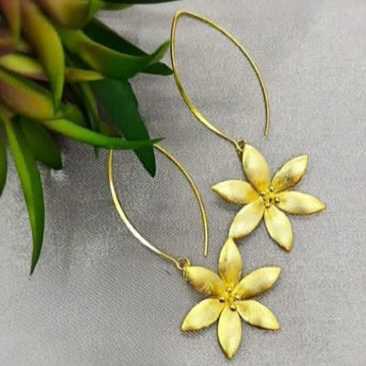 Gold plated on sterling silver daisy-shaped earrings displayed against a neutral background with a green leafy object to the side.