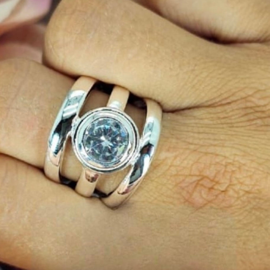 A sterling silver ring with a large cubic zirconia stone, featuring a straight three-line design, worn on a person's finger.