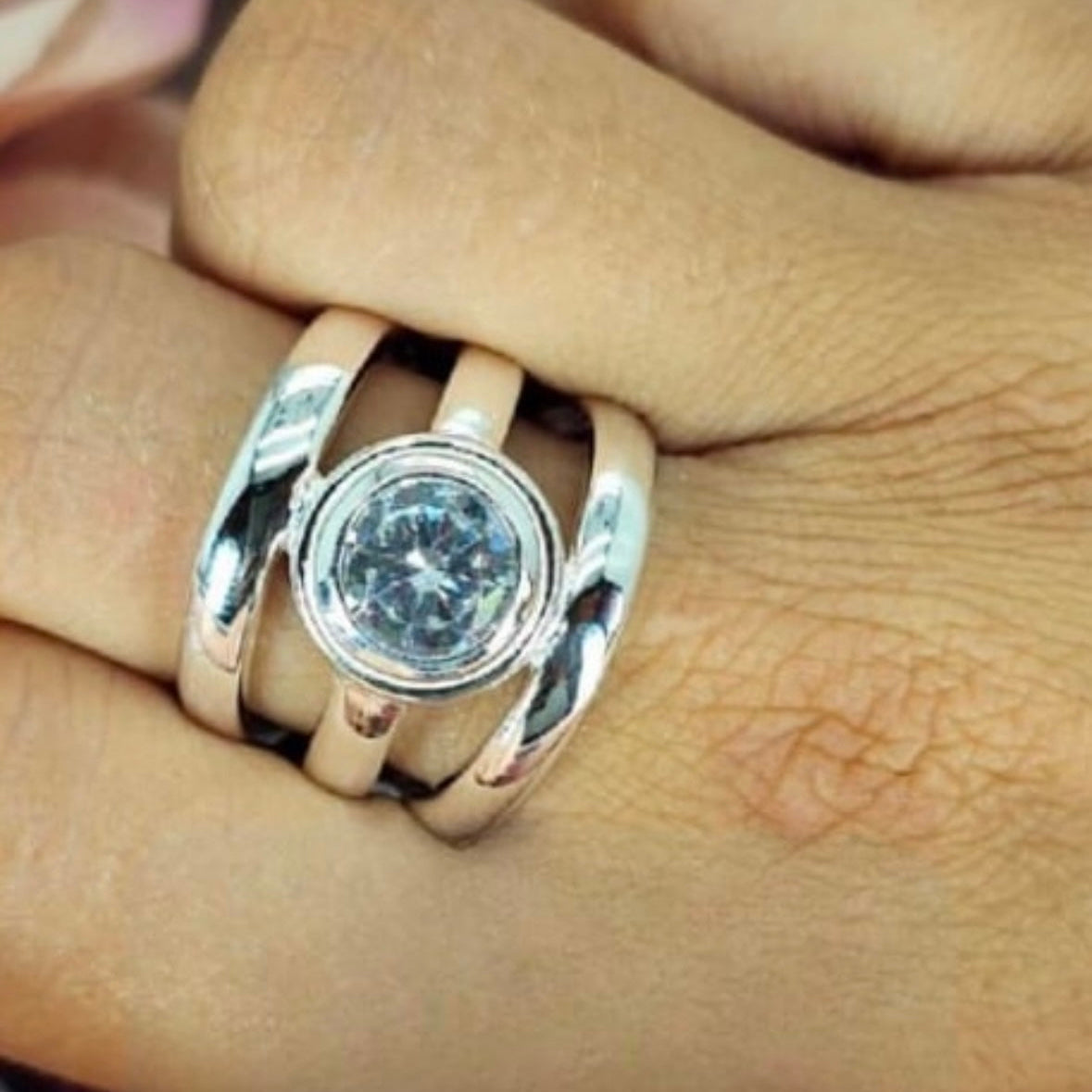 A sterling silver ring with a large cubic zirconia stone, featuring a straight three-line design, worn on a person's finger.
