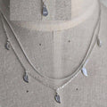 Silver necklace with leaf-shaped pendants on a gray fabric background