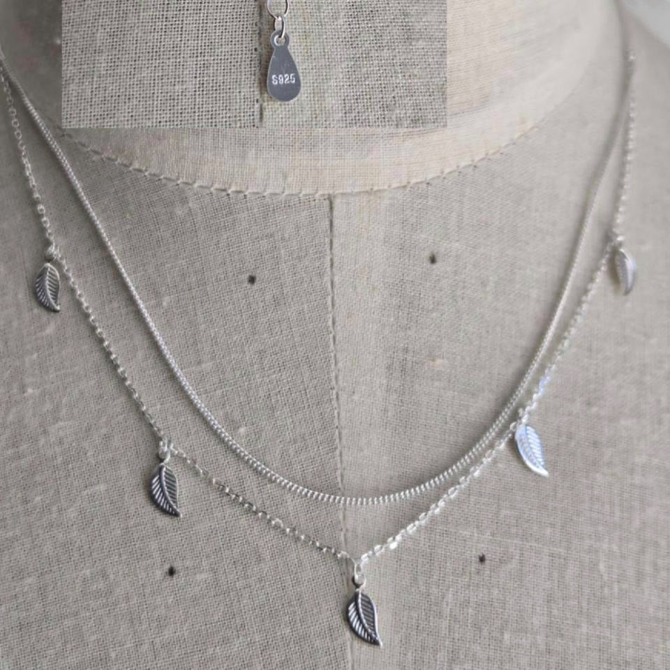 Silver necklace with leaf-shaped pendants on a gray fabric background