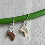 Silver earrings shaped like Africa on a green stick against a textured gray background
