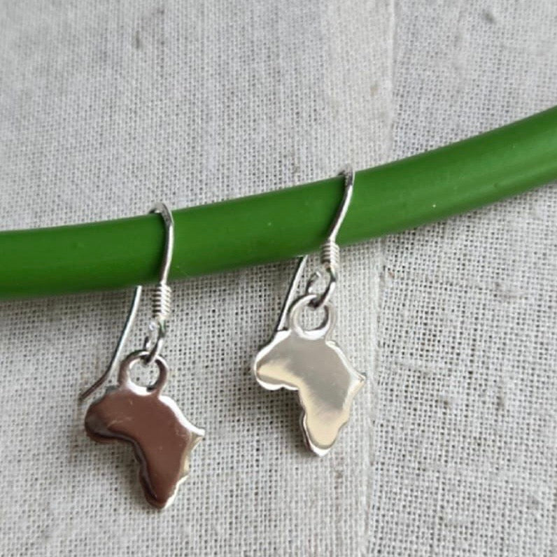 Silver earrings shaped like Africa on a green stick against a textured gray background