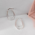 Silver hoop earrings on a light gray surface with a pink mesh bag in the background.