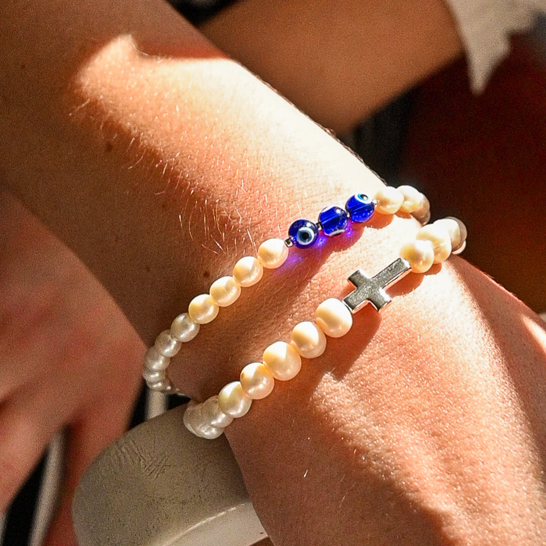 Close-up of a wrist wearing a pearl bracelet with colorful beads and a cross charm.