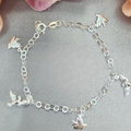 A sterling silver bracelet featuring a series of dangling doves in a chain design, displayed against a floral background.