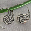 Silver spiral earrings on a green stick with a gray fabric background