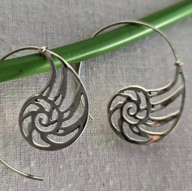 Silver spiral earrings on a green stick with a gray fabric background