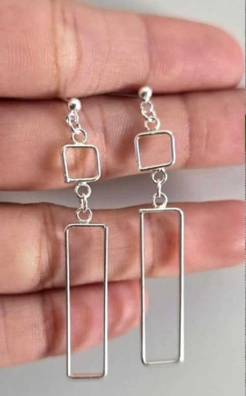 Silver geometric earrings held between fingers against a neutral background