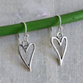 Silver heart-shaped earrings on a green stick against a gray background