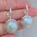 Silver earrings with round moonstone-like stones held between fingers on a light background