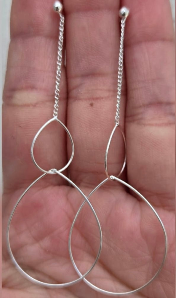 Silver earrings with a unique design held in a hand.