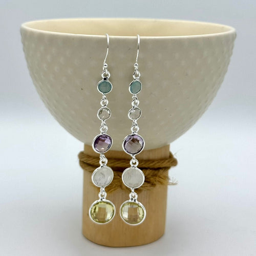 Silver earrings with colorful beads hanging from a ceramic bowl.