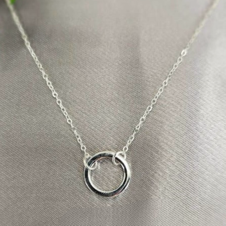 A silver necklace with a simple circle center, displayed on a grey background