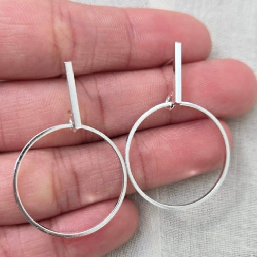 Silver hoop earrings held between fingers on a light background