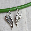 Silver butterfly-shaped earrings on a green stick against a light fabric background