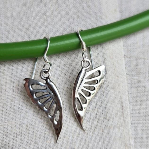 Silver butterfly-shaped earrings on a green stick against a light fabric background