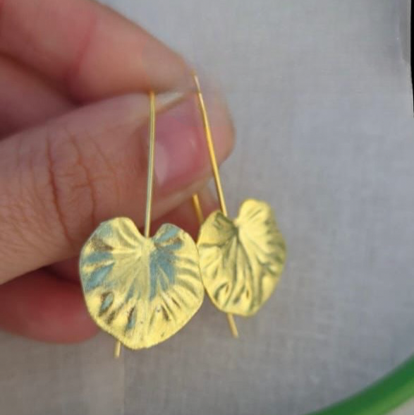 Gold leaf-shaped earrings held by a hand against a white background
