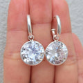 Silver earrings with clear gemstones held between fingers against a neutral background
