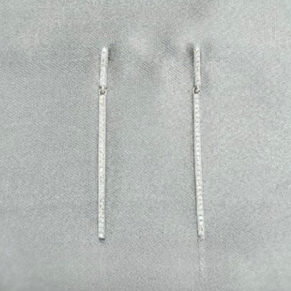 Pair of silver earrings on a gray surface with a soft pink flower in the background.